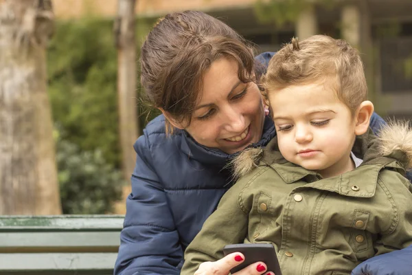 Lindo niño sentado en un banco del parque con su madre — Foto de Stock