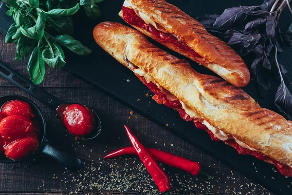 Lång baguette smörgås med sallad, grönsaker, salami, chili och ost på svart bakgrund — Stockfoto