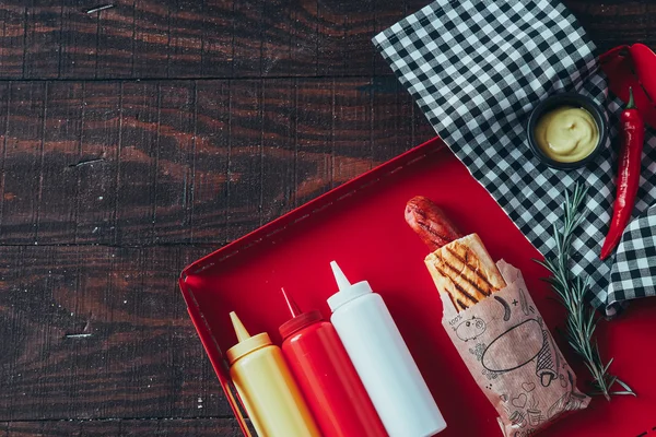 Hot dog with mustard, ketchup and mayonnaise on wooden background. Top view — Stock Photo, Image