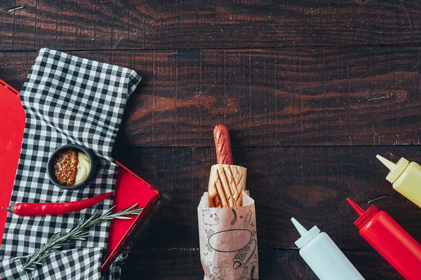Párek v rohlíku s hořčicí, kečupem a majonézou na dřevěné pozadí. Pohled shora — Stock fotografie