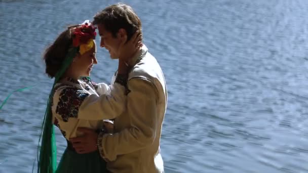 Пара в вышивке, обнимающаяся на берегу реки — стоковое видео