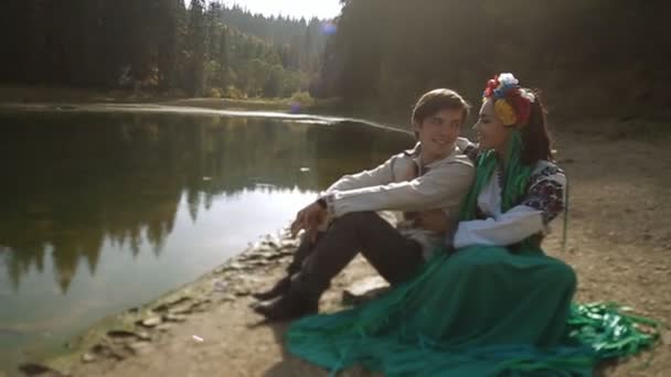 Пара в вышивке сидит на берегу реки — стоковое видео