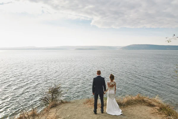 Amantes de la sesión de fotos en un vestido de novia en las montañas cerca de la s —  Fotos de Stock