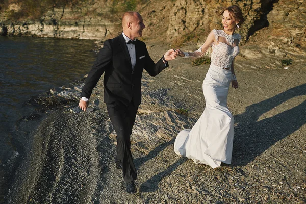 Amantes de la sesión de fotos en un vestido de novia en las montañas cerca de la s — Foto de Stock