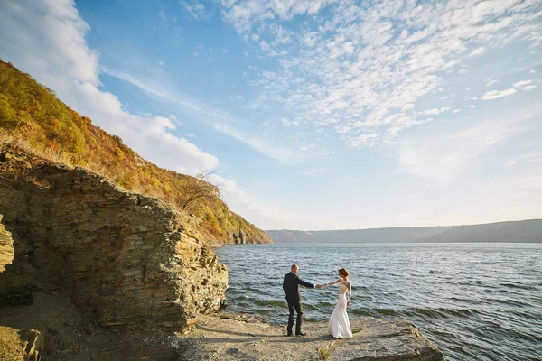 Focení milenců ve svatebních šatech v horách poblíž s — Stock fotografie