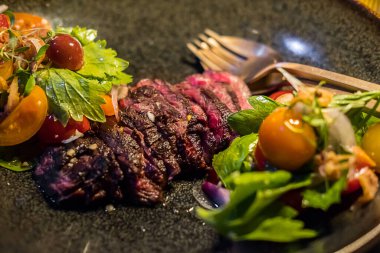 Orta pişmiş et, ahşap tabakta baharatlı salata.