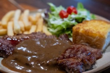 Orta pişmiş biftek, üzerine karabiber sosu, patates kızartması ve ekmek..