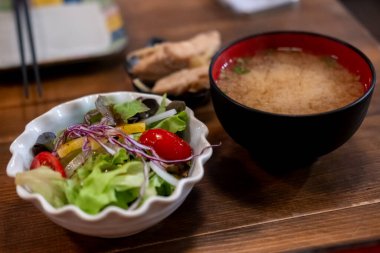 Siyah bir fincanda miso çorbası ile bir kase salata, Japon yemeği. Tahta masada.