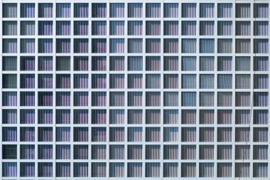 Bir binanın ön cephesinin detaylı bir görüntüsü. Tekrarlanan pencere ve cam blokları, güneş ışığı ve gölgeli.