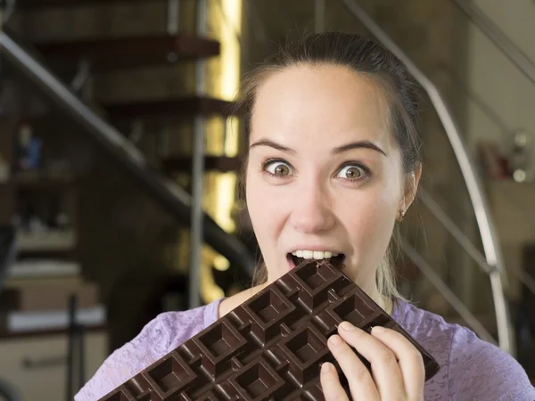 Молодая женщина пытается укусить огромный шоколад — стоковое фото