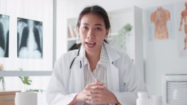 Asyalı kadın doktor kameraya bakar, uzaktan kumandayla hastayla konuşur, reçete yazar. Tele sağlık, tele sağlık, hastane kliniği sağlık hizmetleri, veya internet teknolojisi konsepti