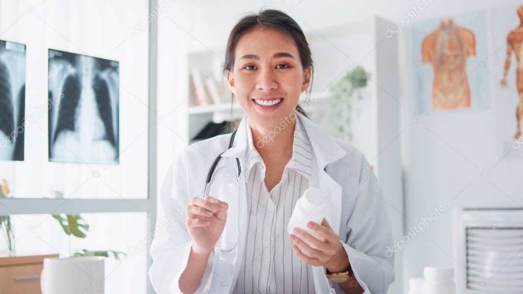 Asian female doctor look at camera, online video call remote talking to patient, prescribe medicine. Tele medical, telehealth, hospital clinic health care service, or internet technology concept