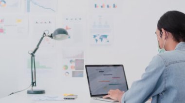 Asyalı iş adamı yüz maskesi takıyor. Ev bilgisayarında çalışıyor. Erkek iş arkadaşıyla dirsek teması kuruyor. Mesafe komitesi, yeni normal ofis, koronavirüs yaşam tarzı konsepti