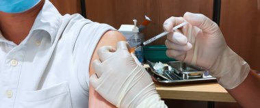 Asyalı adam yüz maskesi takıyor Coronavirus aşısı iğnesini hemşire ya da hastanedeki pratisyen hekim ya da sağlık hizmetlerindeki genel pratisyen tarafından vuruluyor. Aşı olan insanlar ya da Covid-19 pandemik yardım kavramı
