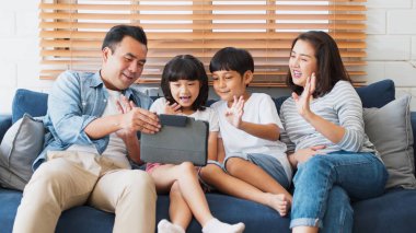 Genç mutlu Asyalı aile dijital tablete el sallıyor, arkadaş veya akraba kuzeniyle çevrimiçi video görüşmesi yapıyor. İnternet bilgi teknolojisi, sosyal uzaklık veya koronavirüs yeni normal yaşam tarzı kavramı