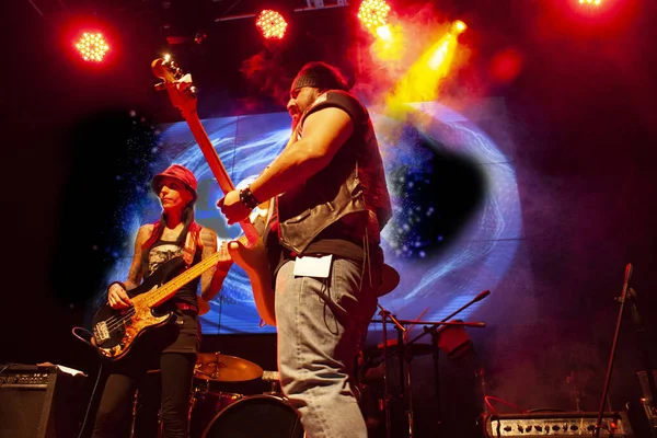 Pair of people woman bassist playing bass strings and man guitarist playing guitar among artificial fog in Mexico city setting nightlife