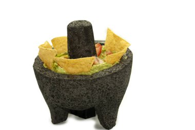 Avokado sosu, yanında kırmızı domateslerle birlikte bir taş kasede tortilla cipsi ile süslenmiş.