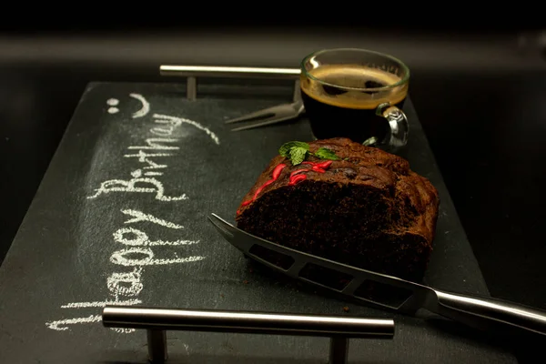 Darck food happy birthday writing chalk chocolate pancake garnished with mint and red glass with coffee to accompany