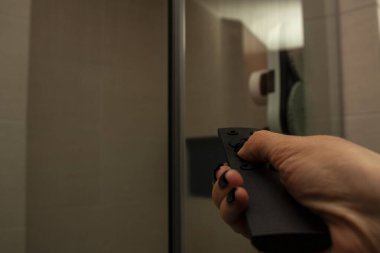 Otomatik temizlik servisine emir vermek için uzaktan kumanda düğmesine basan kadın cam ve duş ekranını temizliyor.