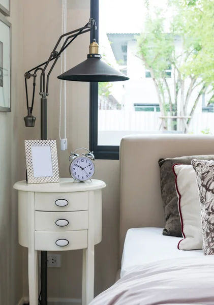 Black lamp, picture frame and alarm clock on bedside table — Stock Photo, Image