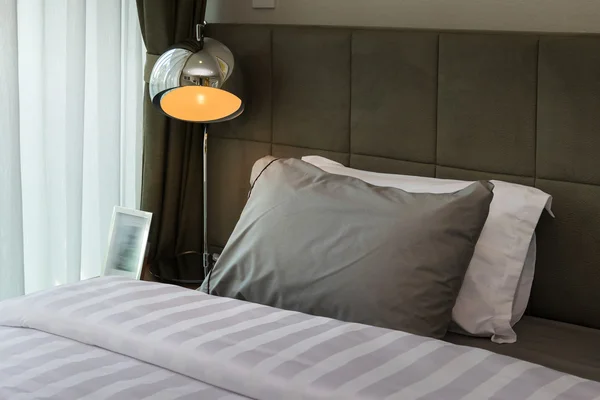 Schreibtischlampe aus Metall und graues Kissen auf dem Bett — Stockfoto