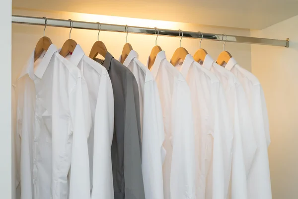 Reihe von weißen und grauen Hemden hängen am Kleiderbügel in weißem Krieg — Stockfoto