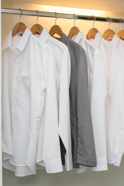 Fila di camicie appese al appendiabiti in armadio bianco — Foto Stock