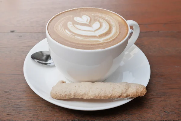 Latte art kawy z serca wzór w białe filiżanka i cookie na drewniane tła — Zdjęcie stockowe