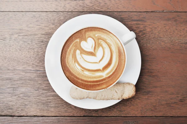 Café arte latte com padrão de coração em uma xícara branca e biscoito no fundo de madeira — Fotografia de Stock