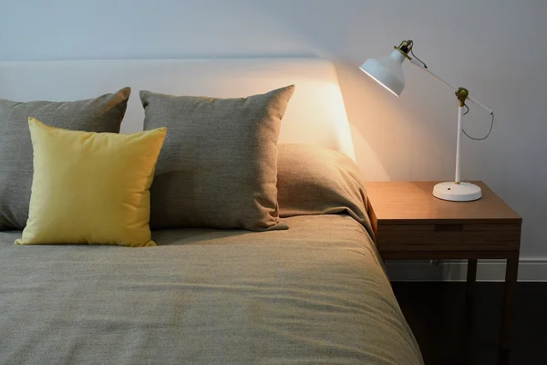 Уютный интерьер спальни с подушками и лампой для чтения на тумбочке — стоковое фото