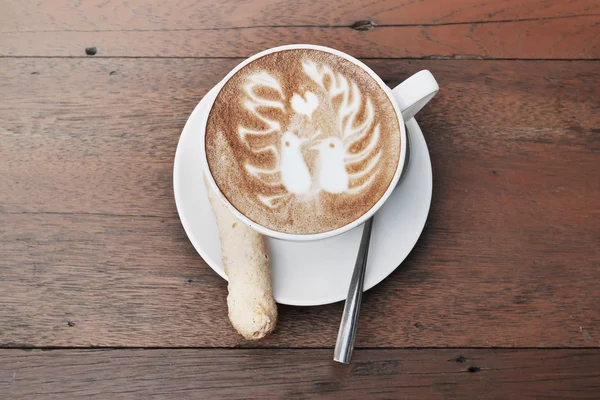 Latte art kawy z dwa ptaki wzór i cookie w filiżance biały na tle drewnianych — Zdjęcie stockowe