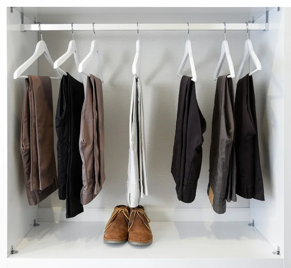 Zapatos de cuero marrón y fila de pantalones negros cuelga en el armario — Foto de Stock