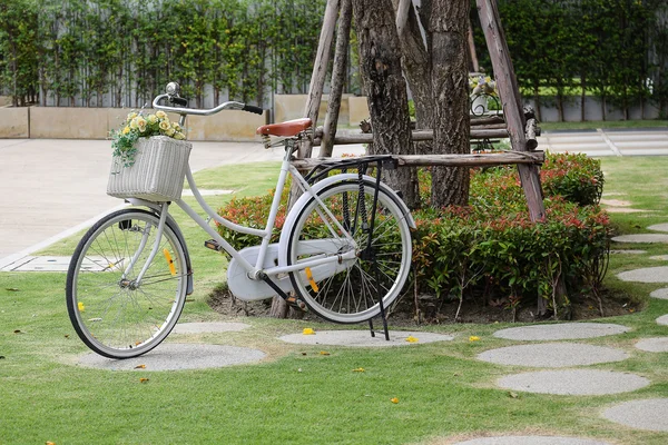 Bicicleta vintage en el jardín con flores artificiales en la cesta — Foto de Stock