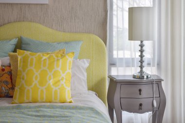 Yellow and green and pattern pillows on classic style bed and reading lamp on bedside table clipart