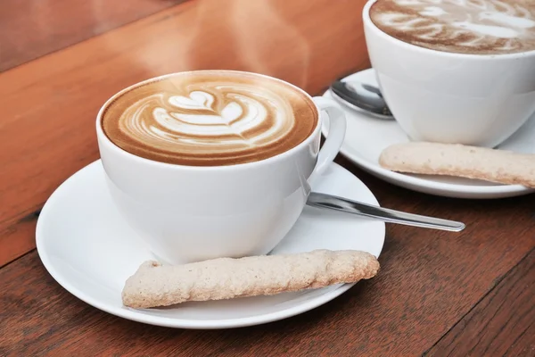 Duas xícaras de café arte latte em uma xícara branca sobre fundo de madeira — Fotografia de Stock