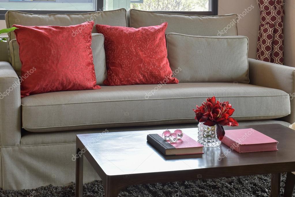 Bequemes Sofa mit roten Kissen und rotem Buch auf Holztisch im
