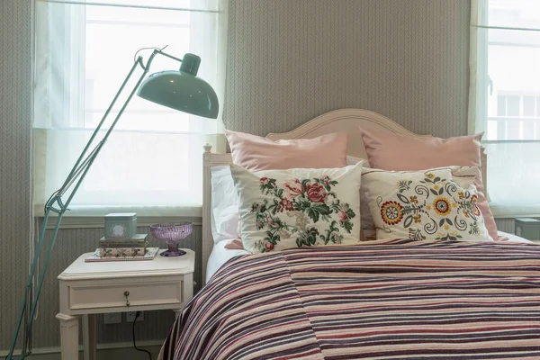 vintage bedroom interior with flower pillows and pink striped blanket on bed