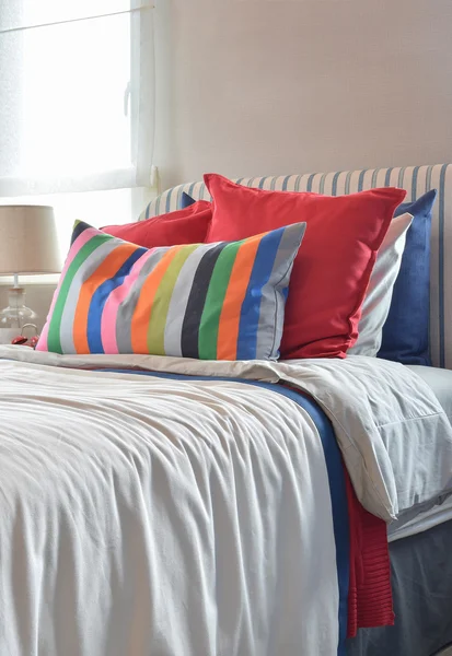 Полосатая спинка кровати с разноцветными подушками и полосатой подушкой на белом простыне — стоковое фото