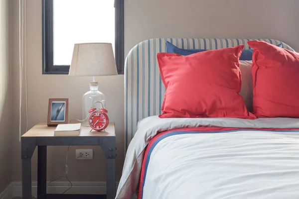 Röda och blå kuddar på den mysiga sängen med randig huvudgavel — Stockfoto