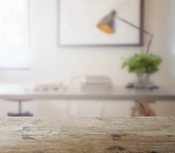 Wooden table top with blur of modern working table with book and lamp as background — Stock Photo, Image