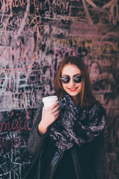 一杯のコーヒーと壁の前に立っているきれいな女の子 — ストック写真