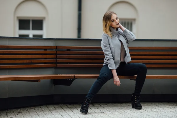 Ung kvinna sitter på bänken framför buindings — Stockfoto