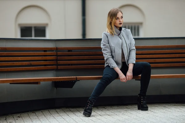 Ung kvinna sitter på bänken framför buindings — Stockfoto