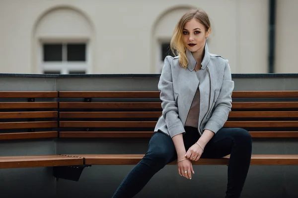 Ung kvinna sitter på bänken framför buindings — Stockfoto