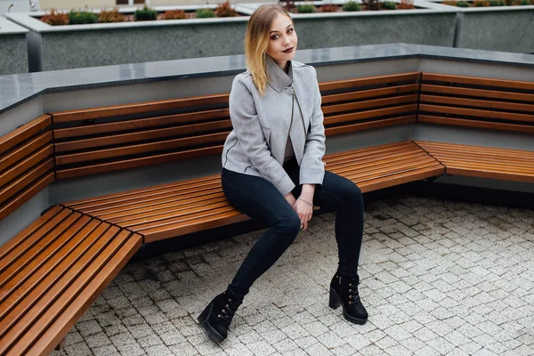 Jonge vrouw zittend op het bankje voor buindings — Stockfoto