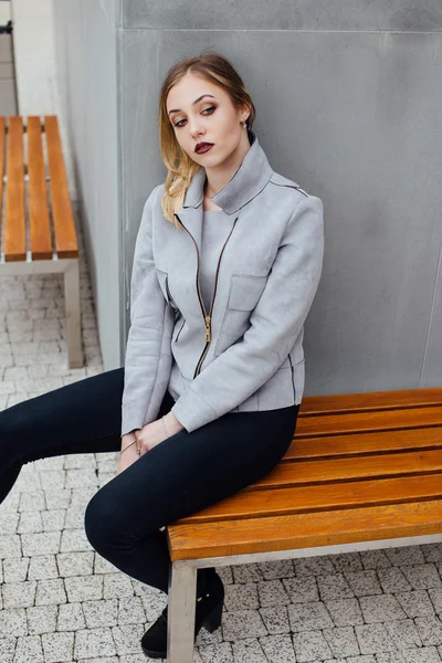 Jovem mulher sentada no banco na frente de buindings — Fotografia de Stock