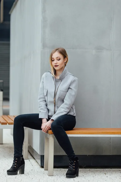 Fiatal nő ül a padon, buindings előtt — Stock Fotó