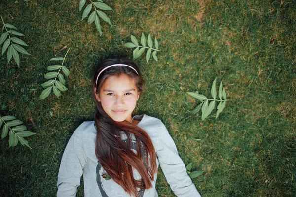 Güzel küçük bir kız çim ve gülümseme üzerinde yalan — Stok fotoğraf