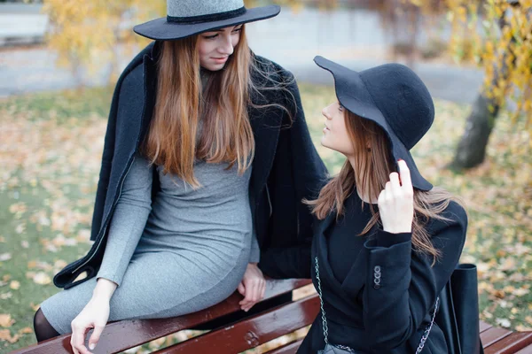 Две молодые девушки сидят на скамейке и позируют перед камерой — стоковое фото