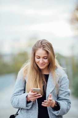 Sokakta yürüyen ve telefon üzerinde sarı saçlı kadın